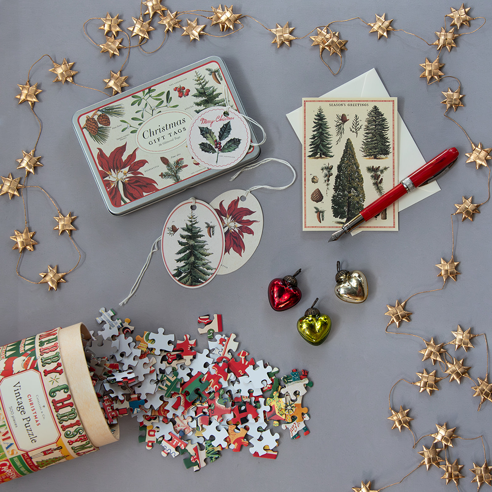 holiday items- puzzle, gift tags, gold star garland, 3 heart shaped ornaments, holiday card with trees, and a red fountain pen