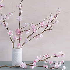 Paper cherry blossoms attached to branches on display in a white vase