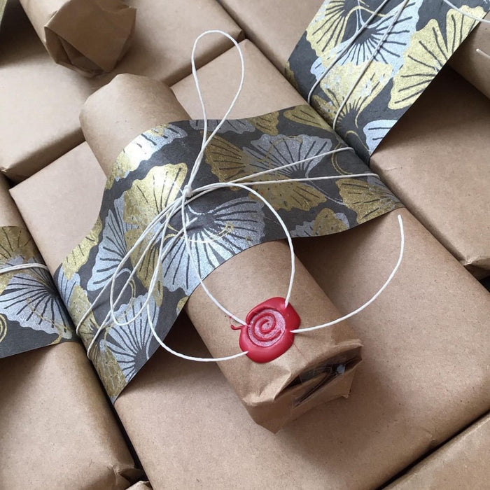 brown paper package with decorative paper strip, white string, and red wax seal.
