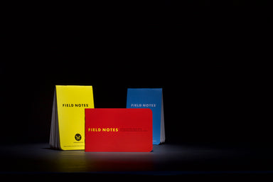 Three Field Notes notebooks in yellow, red, and blue on a black background