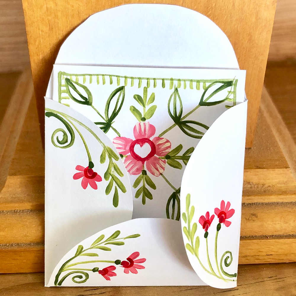 Floral design on a white card with green leaves and pink flowers, placed on a wooden surface.