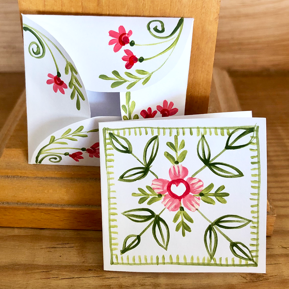 Card and folded envelope with pink flowers and green leaves on a wooden surface.