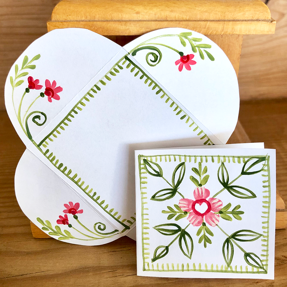 Card and  open envelope with red and green floral design on a wooden surface