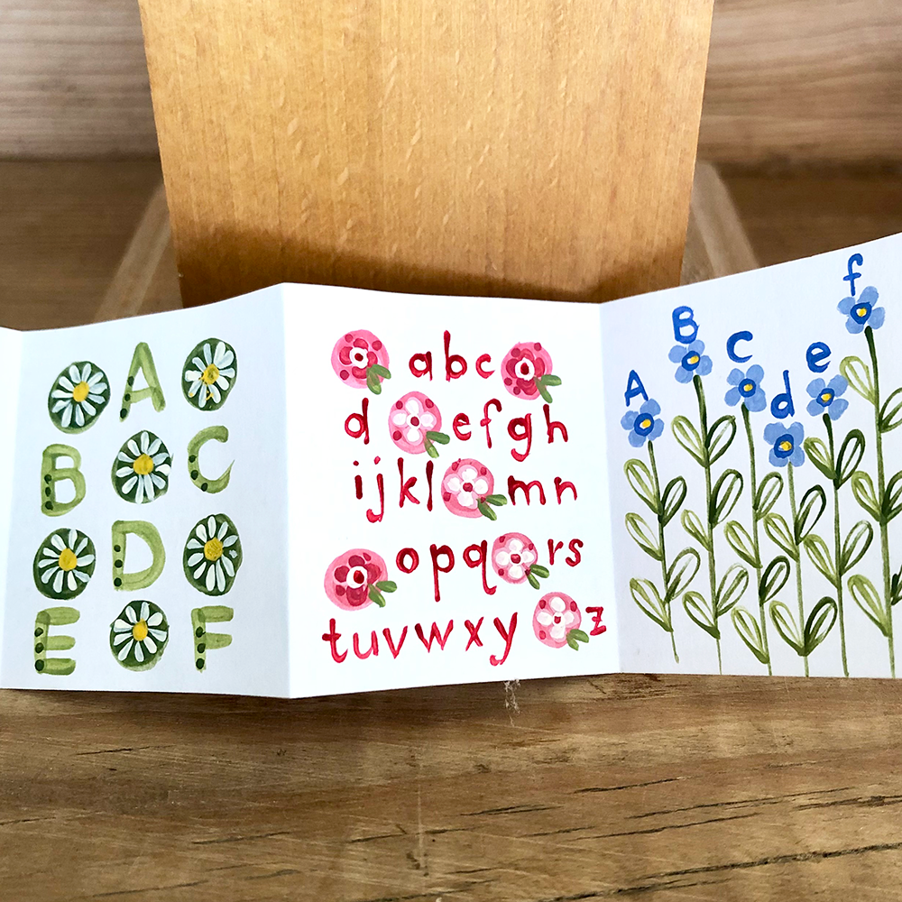Accordion fold book with alphabet and flower illustrations on a wooden surface