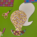 Colorful paper cutout of a hot air balloon with geometric patterns on a green background, accompanied by scissors.