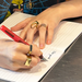 Person writing with a red fountain pen on lined paper, wearing gold rings.