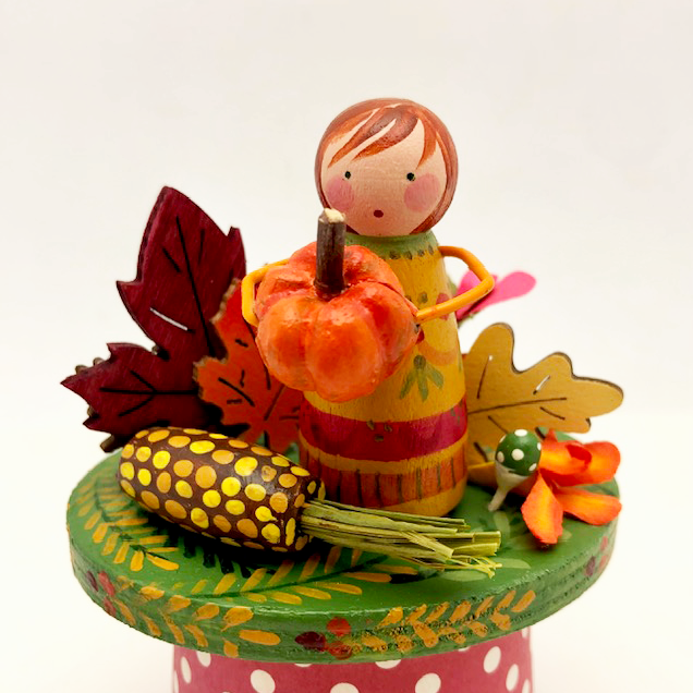 Harvest Girl Class sample with painted peg doll holding miniature pumpkin, corn cob, and leaves