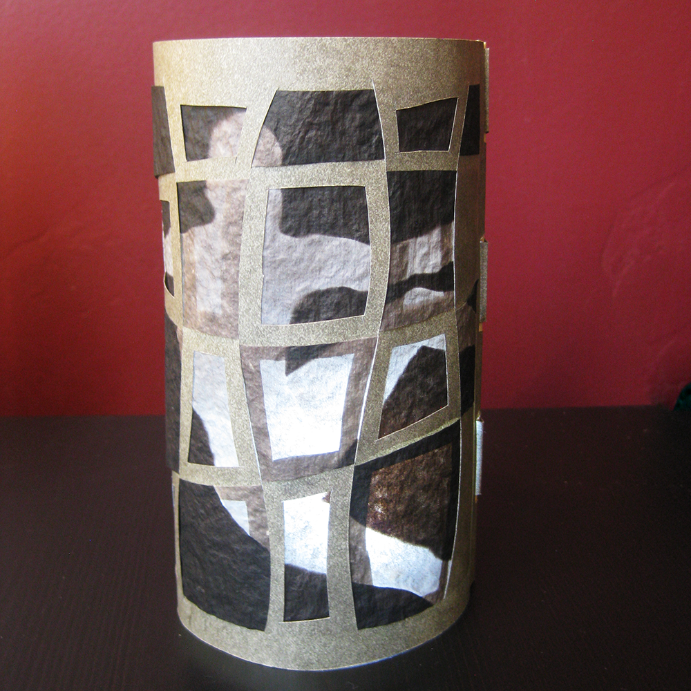 Decorative cylindrical lamp with geometric cutout pattern with figure behind on a red background