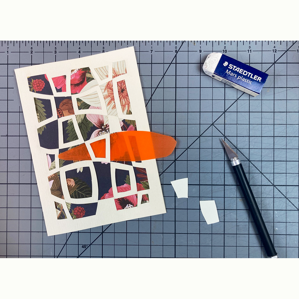 Greeting card with floral design on a white background with cut paper geometric pattern laid on top in the process of cutting with cutting mat, X-acto knife, and eraser