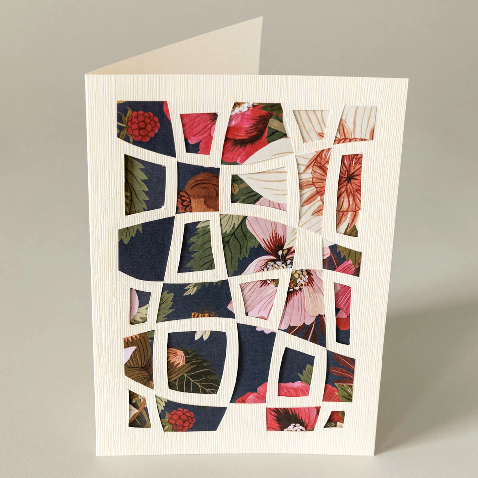 Greeting card with floral design on a white background with cut paper geometric pattern laid on top.