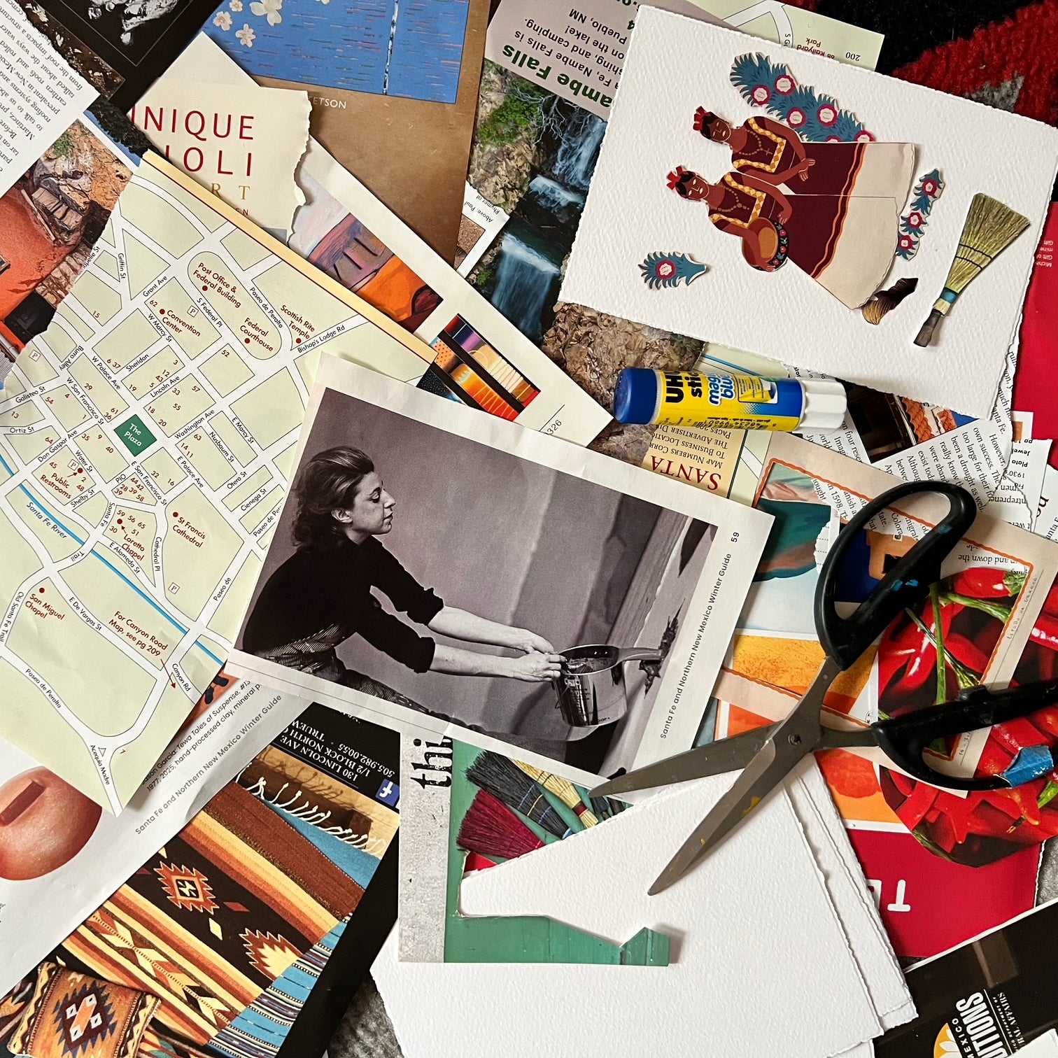 Collage materials of vintage paper cutouts, printed cards, a black-and-white photo print, a map, scissors, and craft supplies arranged on a dark surface.