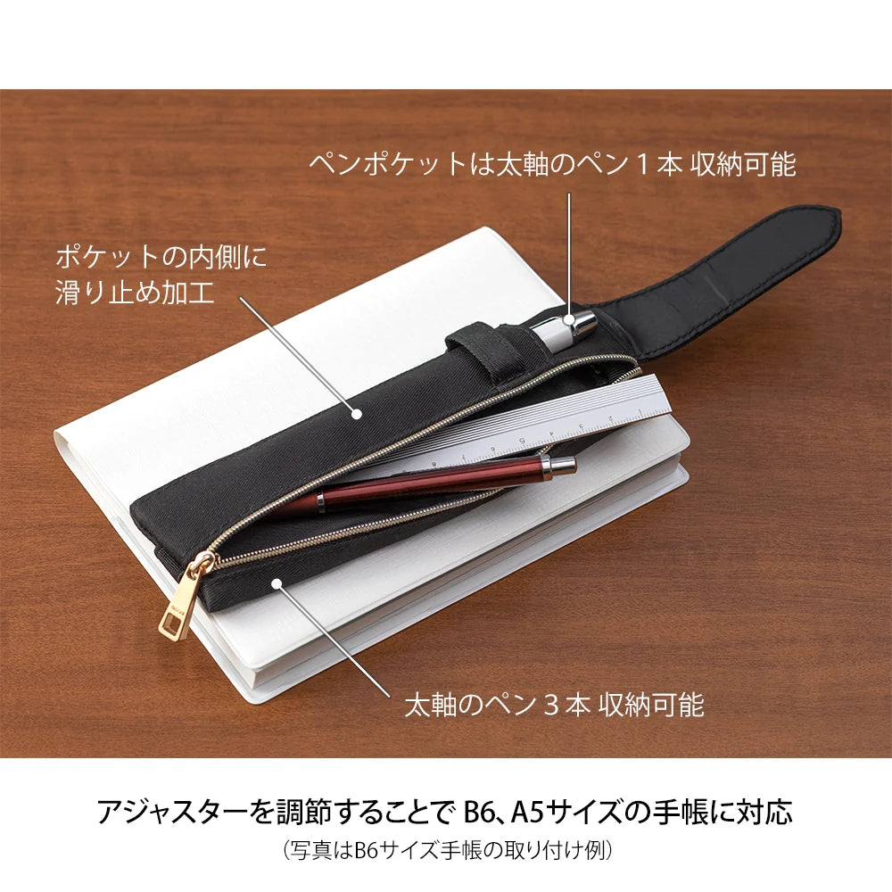 Black pen holder with adjustable strap on a wooden surface