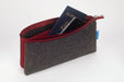 A dark gray felt zippered pouch with a red interior lining, shown open with a blue passport and smartphone inside. 