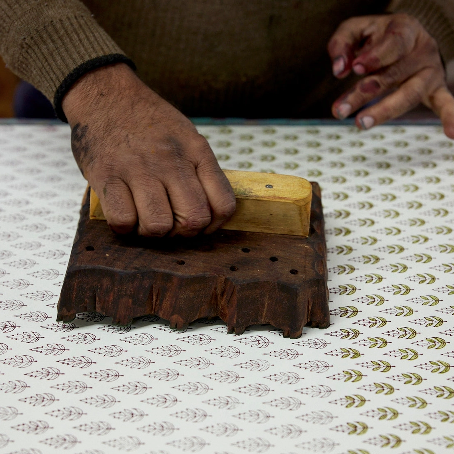 Hand using a wooden stamp creating the repeat floral pattern on paper