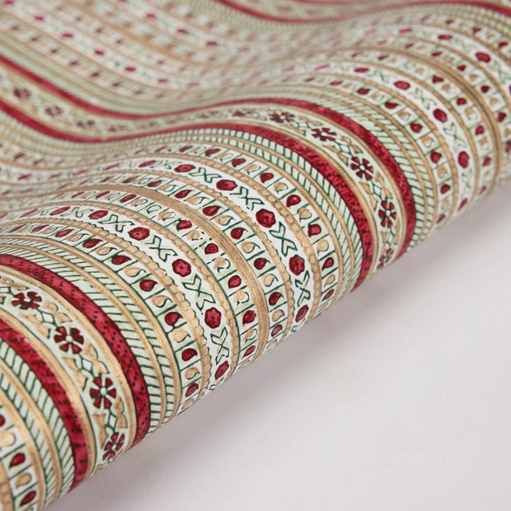 Roll of patterned paper with red, green, and gold patternes on a white background
