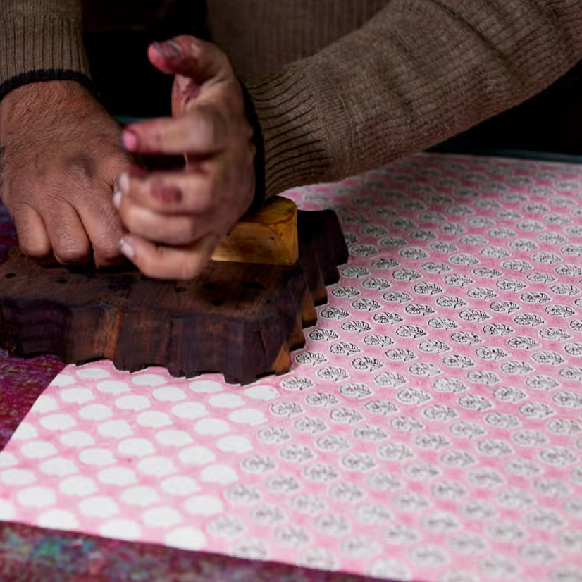Block printing in studio- pink background with hand holding block filling in flower details