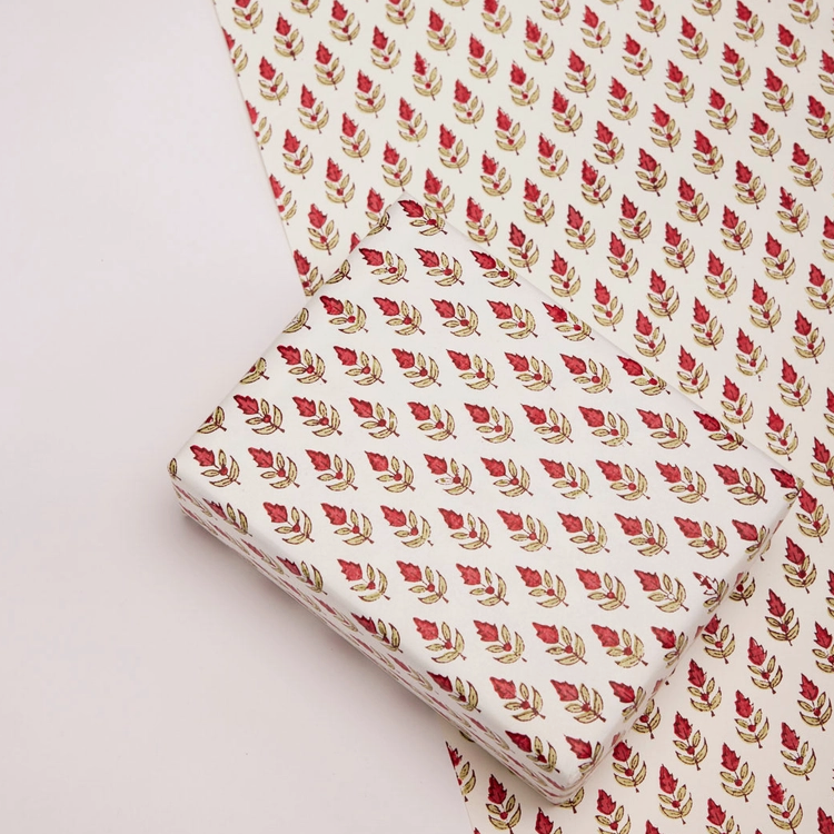Paper with red and green floral and leaf repeat pattern with one flat sheet and a wrapped box with the same pattern
