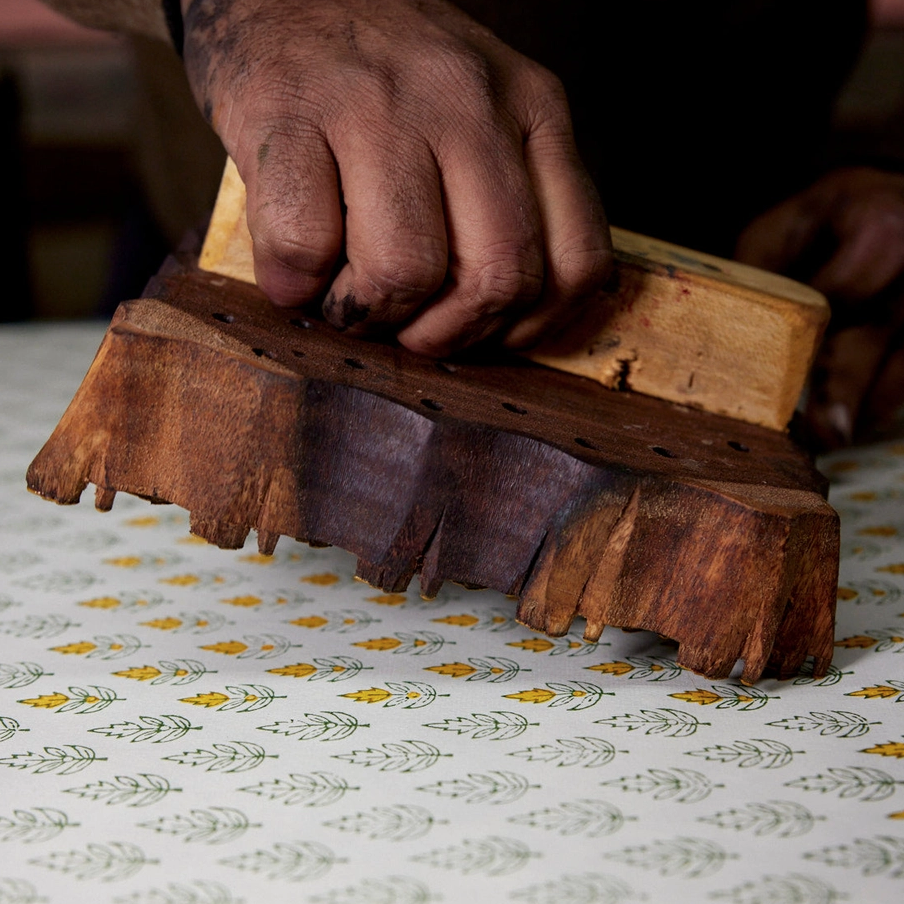 Hand using a wooden printing block on paper creating floral patterns