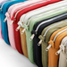 A close-up diagonal arrangement of multiple zippered pouches in assorted colors, including blue, pink, red, white, sage green, black, olive green, mustard, and beige, with silver metal zippers.