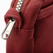 Close-up of a burgundy canvas bag featuring a silver metal zipper pull and a matching fabric loop tab, with a white background visible in the corner.