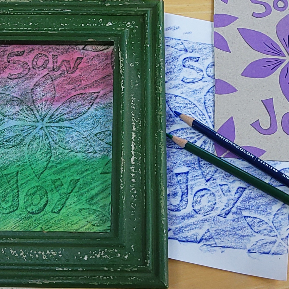 Green framed artwork with 'Sow Joy' text and floral design, next to a pencil and other printed materials.