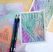 Colorful art cards with heart designs and two colored pencils on a wooden surface