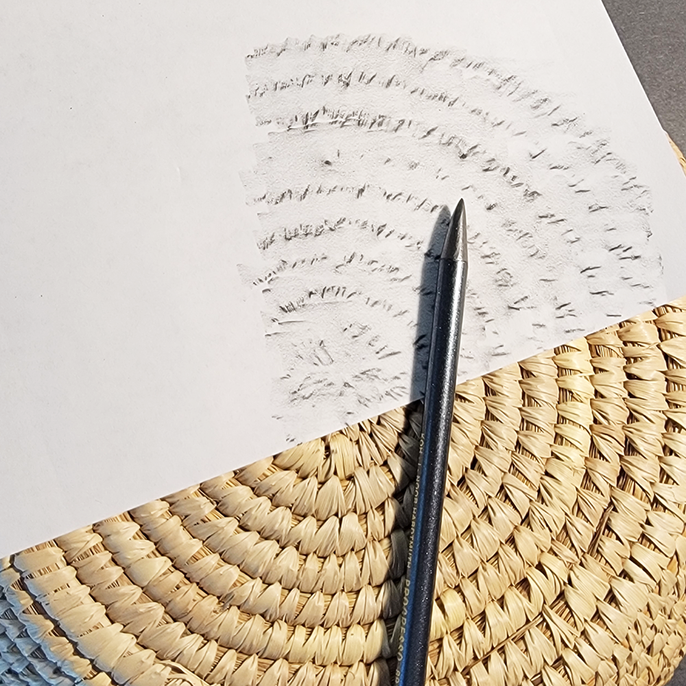 Graphite pencil and white paper on a textured surface with example of texture rubbing