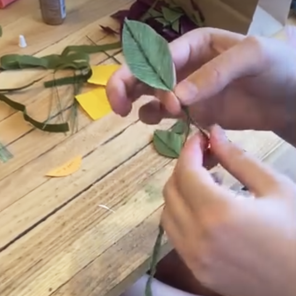 Person assembling a paper leaf on a wire  stem