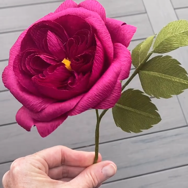 Hand holding a pink crepe paper rose against a wooden background