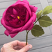 Hand holding a pink crepe paper rose against a wooden background