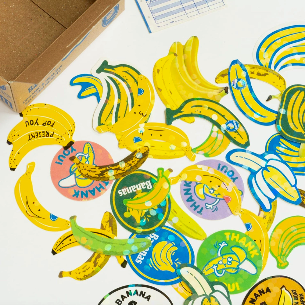 Collection of banana-themed stickers on a white surface with a cardboard box in the background.