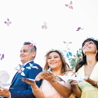 Three people, two women and a man, are smiling and releasing magic butterflies around them at a celebration