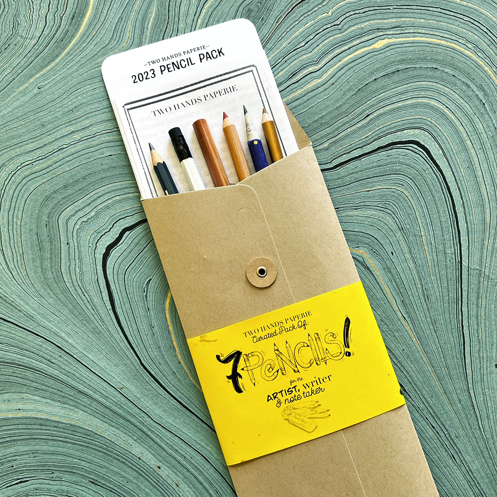 2023 pencil pack in kraft envelope with yellow wrap- shown open on turquoise marbled paper  with included info peeking out of pack